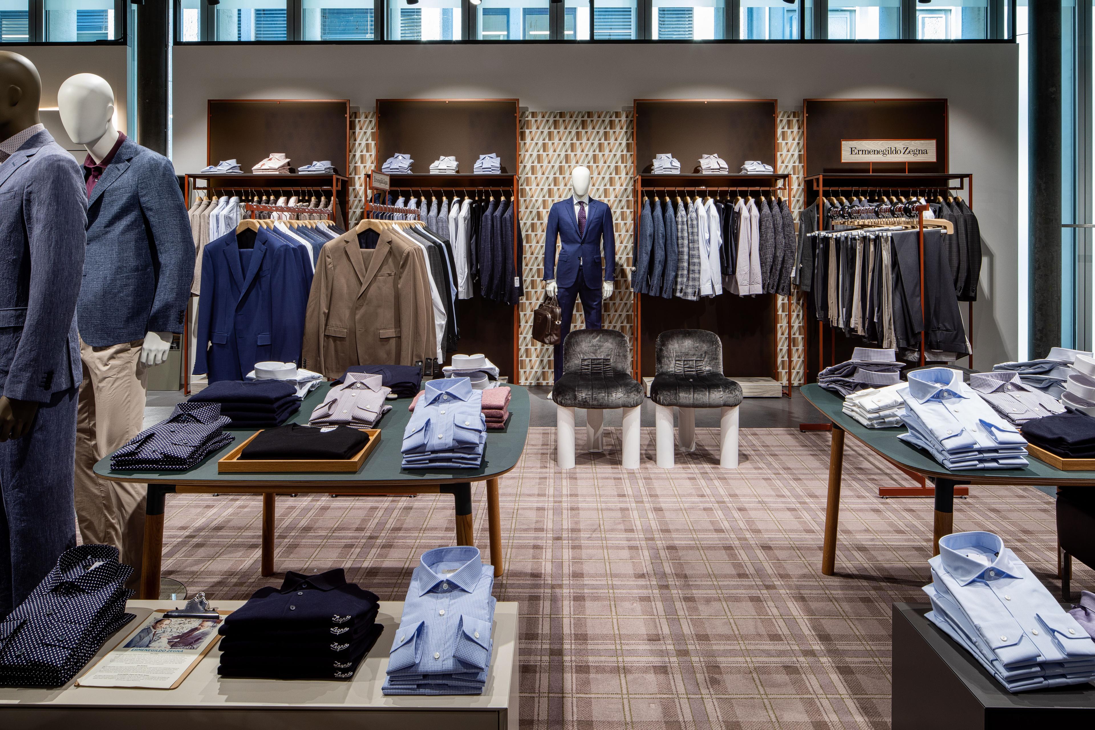 Interior of a men's clothing store with suits, shirts, and mannequins.