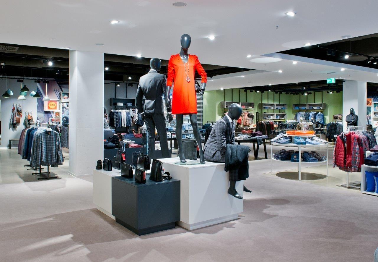 Mannequins displaying clothing in a brightly lit department store, one wearing a vibrant red coat.