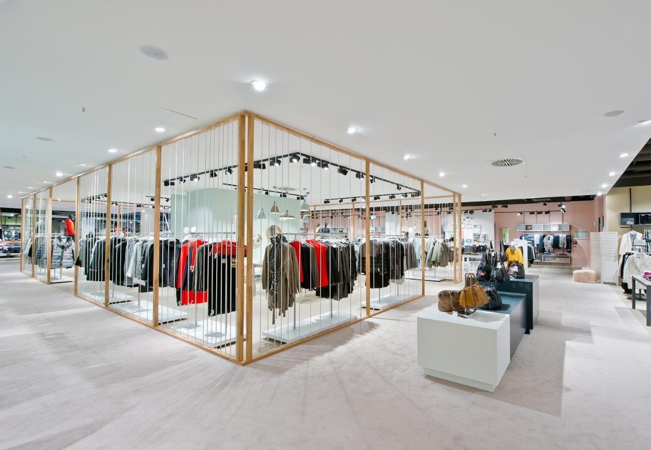 Modern clothing store interior featuring racks of apparel within a gold-framed display structure.