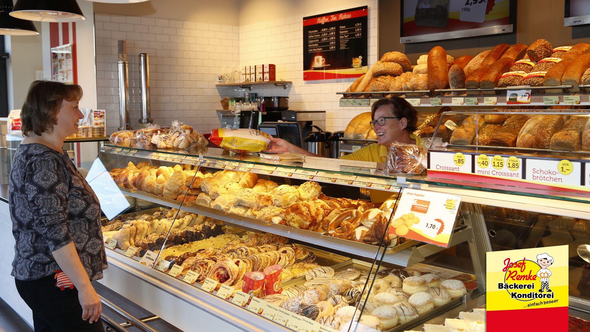 Customer at a bakery counter receives an item from a baker, surrounded by fresh pastries.