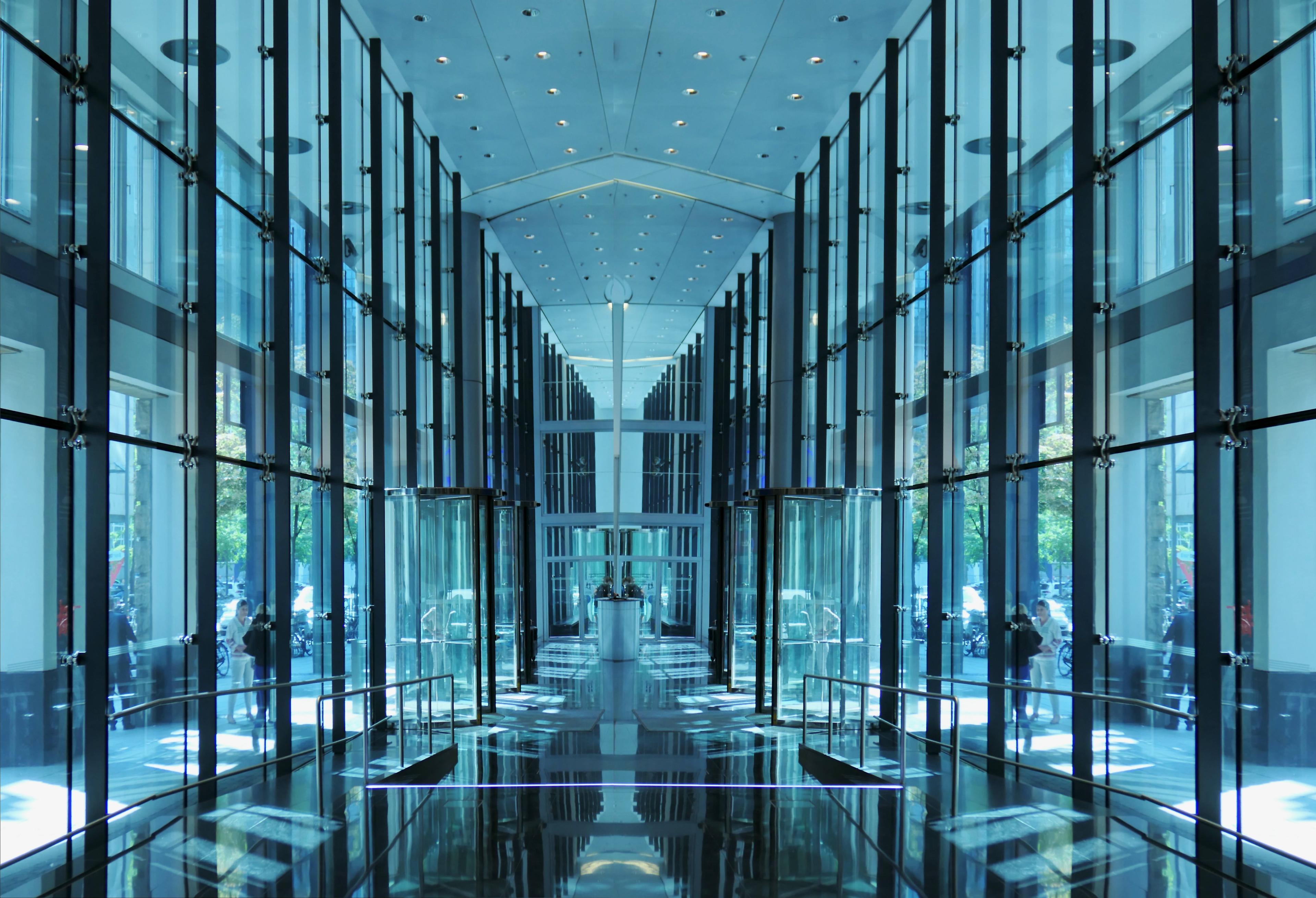 Modern building interior with symmetrical glass walls, reflective floor, and a high ceiling.